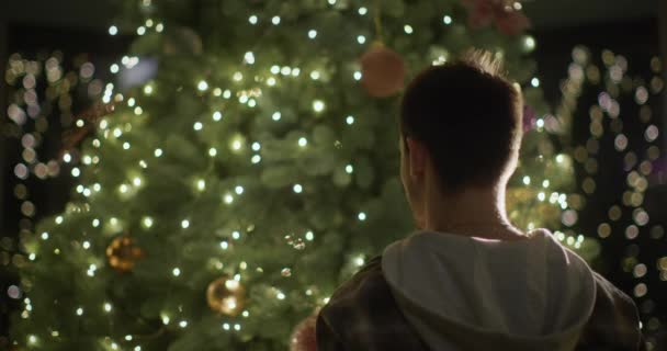 一个年轻人在家里装饰圣诞树 挂一个玩具 — 图库视频影像