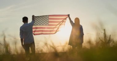 Erkek ve kadın gün batımında buğday tarlasının üzerinde Amerikan bayrağını dalgalandırıyor. ABD 'nin bağımsızlık günü kavramı.