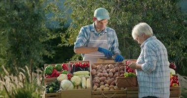 Yaşlı bir kadın pazardan sebze alır, satıcı sebzeleri sepetine koyar. 4k video