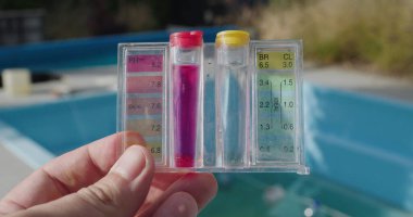 Bir adam yüzme havuzunun arka planına karşı PH ve klor seviyeleri için test cihazı tutuyor. Su Kalite Testi.