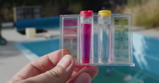 男性はプールの背景に対してPhと塩素レベルのテスターを保持します 水質のテスト — ストック動画