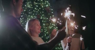 Mutlu bir aile yılbaşını Noel ağacında kutluyor, elinde yanan maytaplar var..