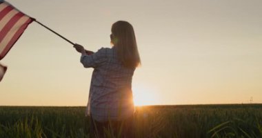 Buğday tarlasında Amerikan bayrağı sallayan mutlu kadın. 4 Temmuz - Bağımsızlık Günü ABD konsepti.