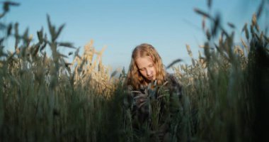 A teenage girl with long hair and a bouquet of spikelets of wheat sits in a wheat field. Summer on the farm.