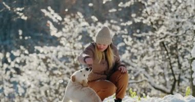 Genç bir kadın açık bir kış gününde karlı bir parkta Golden Retriever 'ıyla oynuyor..