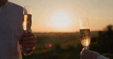 Kırmızı şarap kadehleriyle genç çift resimli bir vadide gün batımını seyrediyor..