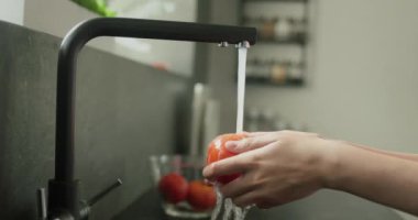 Kadınların elleri, mutfak musluğundan gelen su püskürtülerinin altında olgun kırmızı bir domates yıkar..