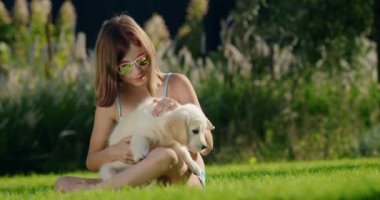 Bir çocuk evin arka bahçesinde bir köpek yavrusuyla oynuyor. Manikürlü çimlerde otururken.