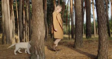 Köpekli bir kadın ormanda uzun çam ağaçlarının arasında yürüyor..
