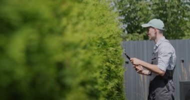 Tulumlu genç bahçıvan bahçedeki ağaçları kesiyor..