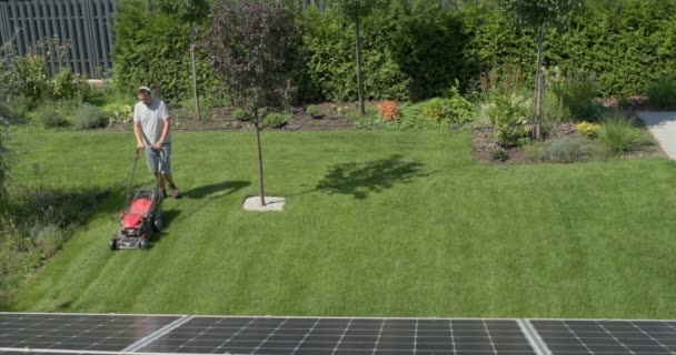 一个男人在房子的院子里修剪草坪 用耳机听音乐 4K视频 — 图库视频影像