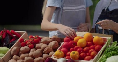 Bir kadın ve torunu markette sebze satıyorlar, domatesleri kese kağıdına koyuyorlar. Çerçevede sadece eller görünüyor..