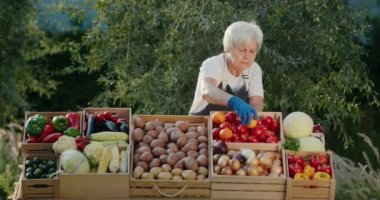 Çiftçi pazarında yaşlı bir kadın satıcının portresi. Yerel sebzelerle tezgahın arkasında dikiliyorum..