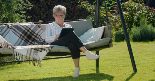 Porträtt Äldre Kvinna Som Använder Tablett Sitter Trädgårdsgunga Baksidan Ett — Stockvideo