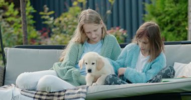 İki kız evin arka bahçesinde salıncakta oturan bir köpek yavrusuyla oynuyorlar. 4k video