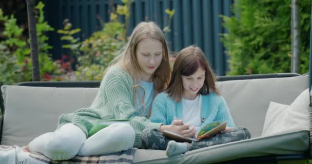 两个女孩看书 坐在自家后院的花园秋千上 — 图库视频影像