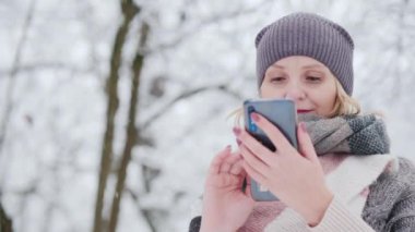 Young woman uses smartphone in snow park.
