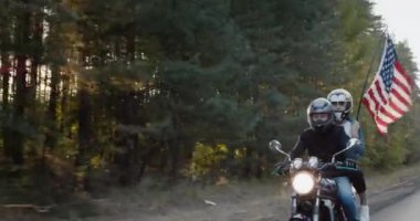 Motosiklet süren bir adam, Amerikan bayrağı taşıyan bir kız..