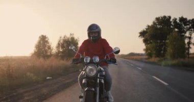 Motosikletli bir motorcunun silüeti, gün batımının ışınlarında otoyolda gidiyor..