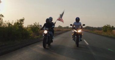 Bir grup motorcu gün batımında otoyol boyunca Amerika bayrağıyla ülkeyi turluyor..