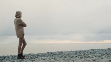 A woman in a warm knitted sweater looks at the sea where the storm begins.