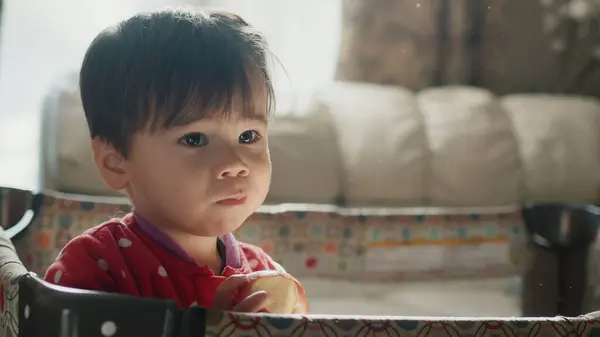 2歳のアジア系の子供がリンゴを食べベビーベッドに立っています ロイヤリティフリーのストック写真