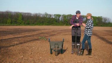 İki çiftçi konuşuyor. Bir tarlada tohum tohumu taşıyan el arabasının yanında duruyorum..