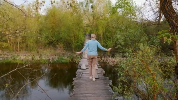 Seorang Wanita Berjalan Melintasi Jembatan Gantung Yang Tipis Atas Sungai — Stok Video