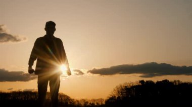 Renkli gökyüzü ve bulutlarla çevrili çarpıcı bir günbatımının önünde huzur içinde duran bir adamın silueti doğayla uyum içinde neşeli bir jest sergiliyor.