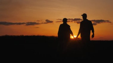 Batan güneşin arka planında, bir çift çimen tarlasında el ele durur.