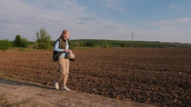 Bir kadın çiftçi tarlaların arasında köy yolunda yürüyor..