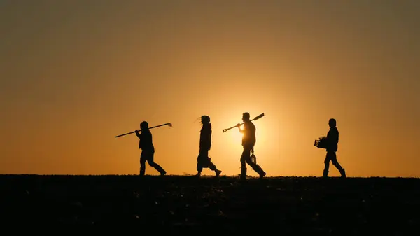 道具を持った農家の家族が畑を歩いています 日没のシルエット ストック写真