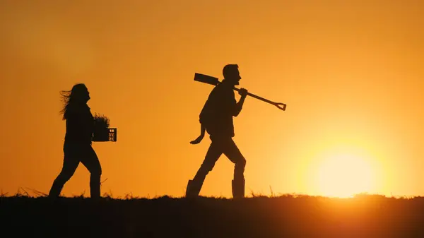 装備を備えた農民のカップルが日没のフィールドを歩いている ロイヤリティフリーのストック写真