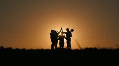 Bir grup çiftçi gün batımında bir tarlada duruyor, beşlik bir hareketle ellerini vuruyorlar. Takım çalışması konsepti