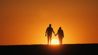 El ele tutuşan genç bir çift, batan güneşe doğru ilerleyen bir tarlada birlikte yürür.