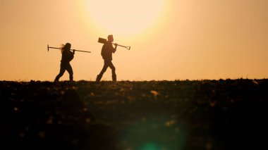 Tarlada yürüyen iki çiftçinin siluetleri güzel bir günbatımının arkaplanına karşı.