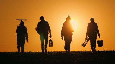 Bir çiftçi ailesi gün batımına doğru tarladan geçiyor. Tohum ekmek için tarımsal araçlar taşıyorum..