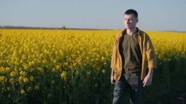 Kendine güveni tam genç bir çiftçi, çiçek açan bir kolza tarlası boyunca yürüyor..