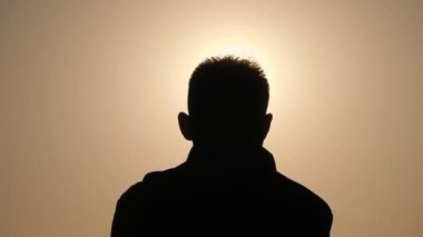 Güneşin parladığı gökyüzünün arka planında bir adamın silueti. Kafasındaki kıllar bir halo gibi çizilmiş..