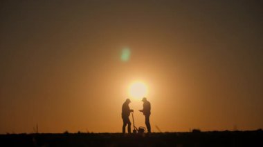 Gün batımında tarlada iletişim kuran ve tablet kullanan iki çiftçinin siluetleri. Yüksek kalite 4k görüntü