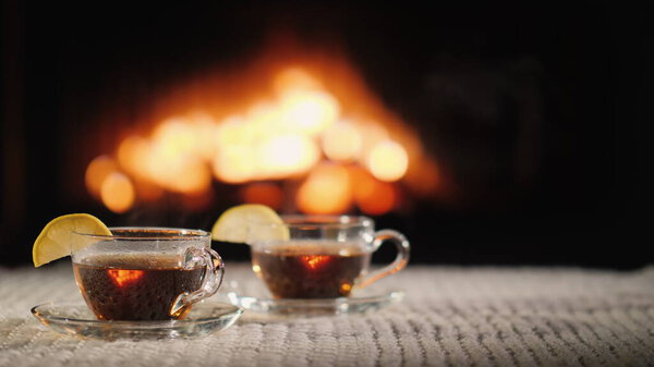 Two cups of hot tea with lemon on a table against the background of the fireplace.