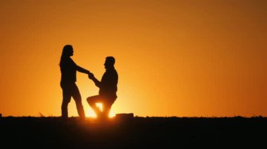Gün batımında romantik bir çiftin siluetleri. Bir adam evlenme teklif eder..