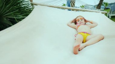Bikinili, yüzü boyalı havalı bir kız yaz tatilinde hamakta dinleniyor..
