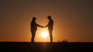 İki çiftçinin siluetleri bir tarlanın üzerinde güneşin arka planına karşı el sıkışıyor. Yüksek kalite fotoğraf
