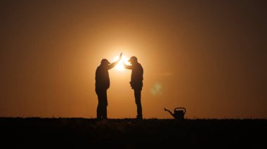 İki çiftçinin siluetleri bir tarlanın üzerinde güneşin arka planına karşı el sıkışıyor. Yüksek kalite fotoğraf