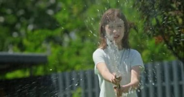 Neşeli bir kız sıcak bir günde bahçe hortumuyla eğleniyor. Etrafa su püskürtüyor, neşeli ve ferahlatıcı bir sahne yaratıyor. Gülüşü ve neşeli hareketleri kaygısızlığın özünü yakalıyor.