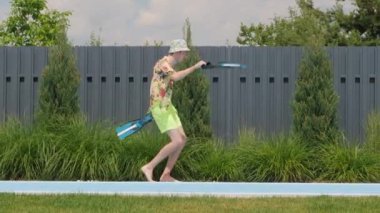 Bir adam coşkuyla yüzme havuzunun kenarında dans ediyor, elinde bir çift palet tutuyor. Onun canlı ve enerjik dans hareketleri, büyük bir gülümsemeyle birleşince,