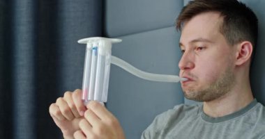 Genç bir adam akciğer fonksiyonlarını değerlendirmek için spirometre kullanırken görülüyor. Bu tıbbi cihaz nefes alıp verebileceği hava miktarını ölçerek solunum sağlığı hakkında hayati veriler sağlıyor. Şey...