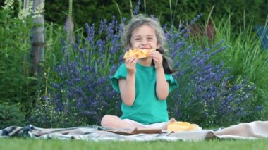 Neşeli bir kız, doğaçlama bir piknikte bir dilim pizzayı hevesle yerken görülüyor. Onun keyifli ifadesi sıradan bir açık hava yemeğinin zevkini yakalıyor..