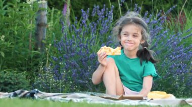 Neşeli bir kız arka bahçedeki çimlerin üzerinde oturmuş bir dilim pizza yerken görülüyor. Sahne, rahat ve keyifli bir an yakalar.. 